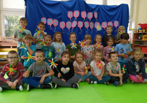 Dzieci z wykonanym przez siebie kwiatkiem pozują do zdjęcia grupowego na tle dekoracji.
